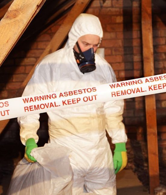 A worker wearing protective clothing while clearing the hazardous substance,asbestos,from an old attic.